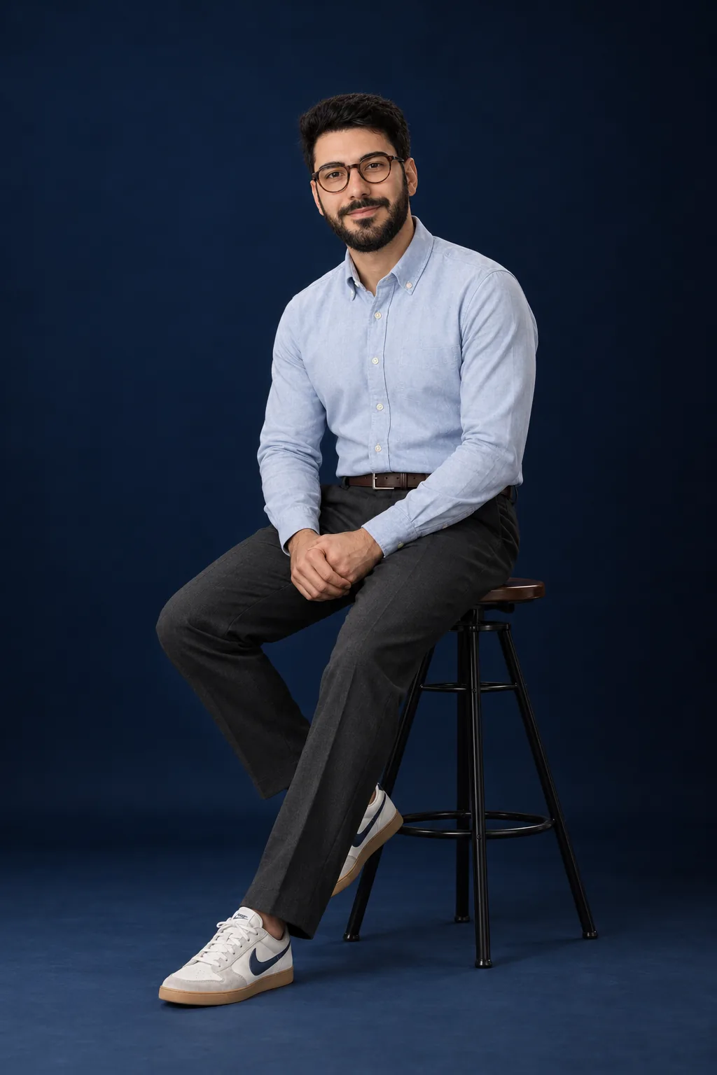 Gabriel Espinheira on a bar stool in the navy studio, hands clasped over his knee, smiling at the camera